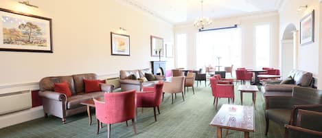 A hotel lounge with leather sofas, red chairs, and a green carpeted floor.