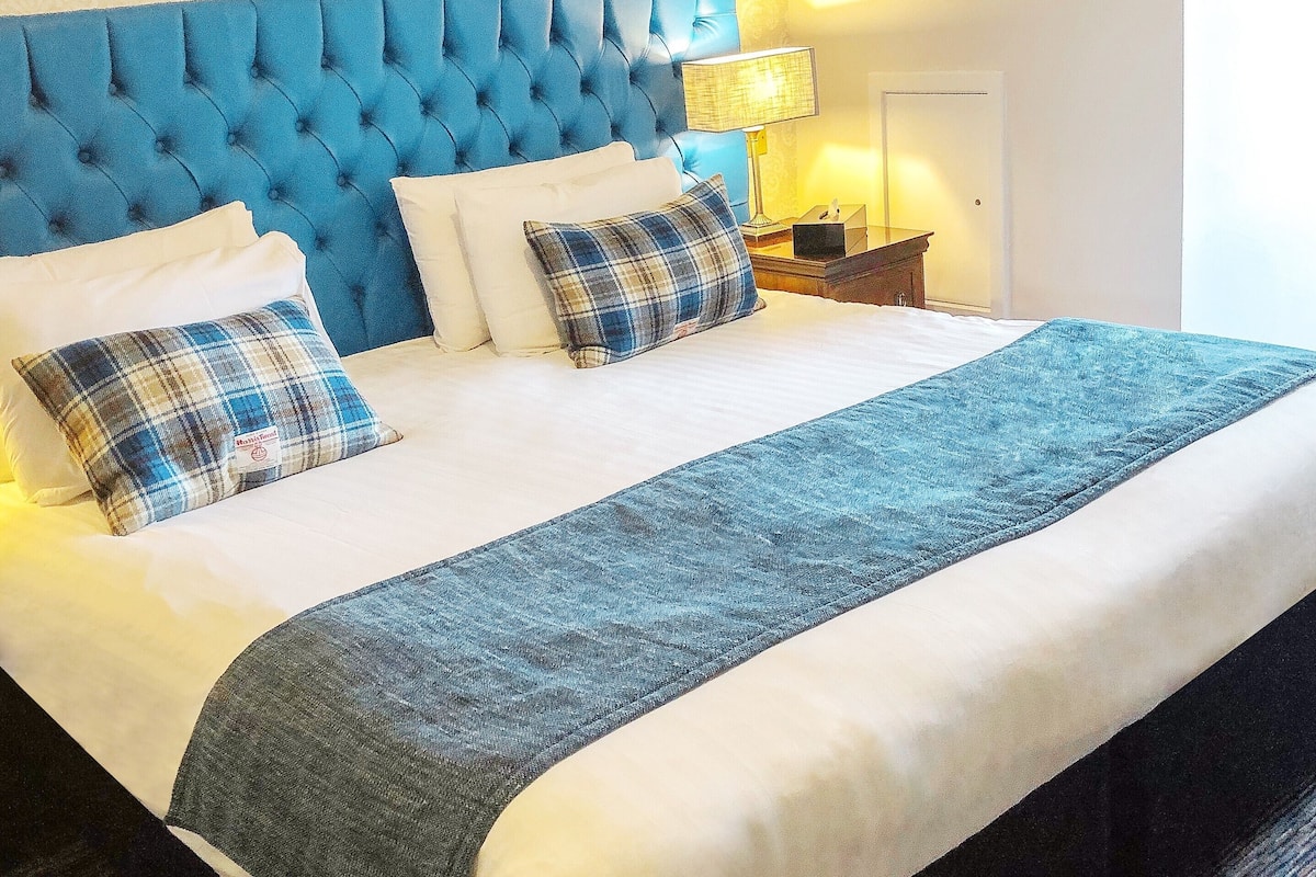 A neatly made bed with a blue headboard, white bedding, and plaid pillows.