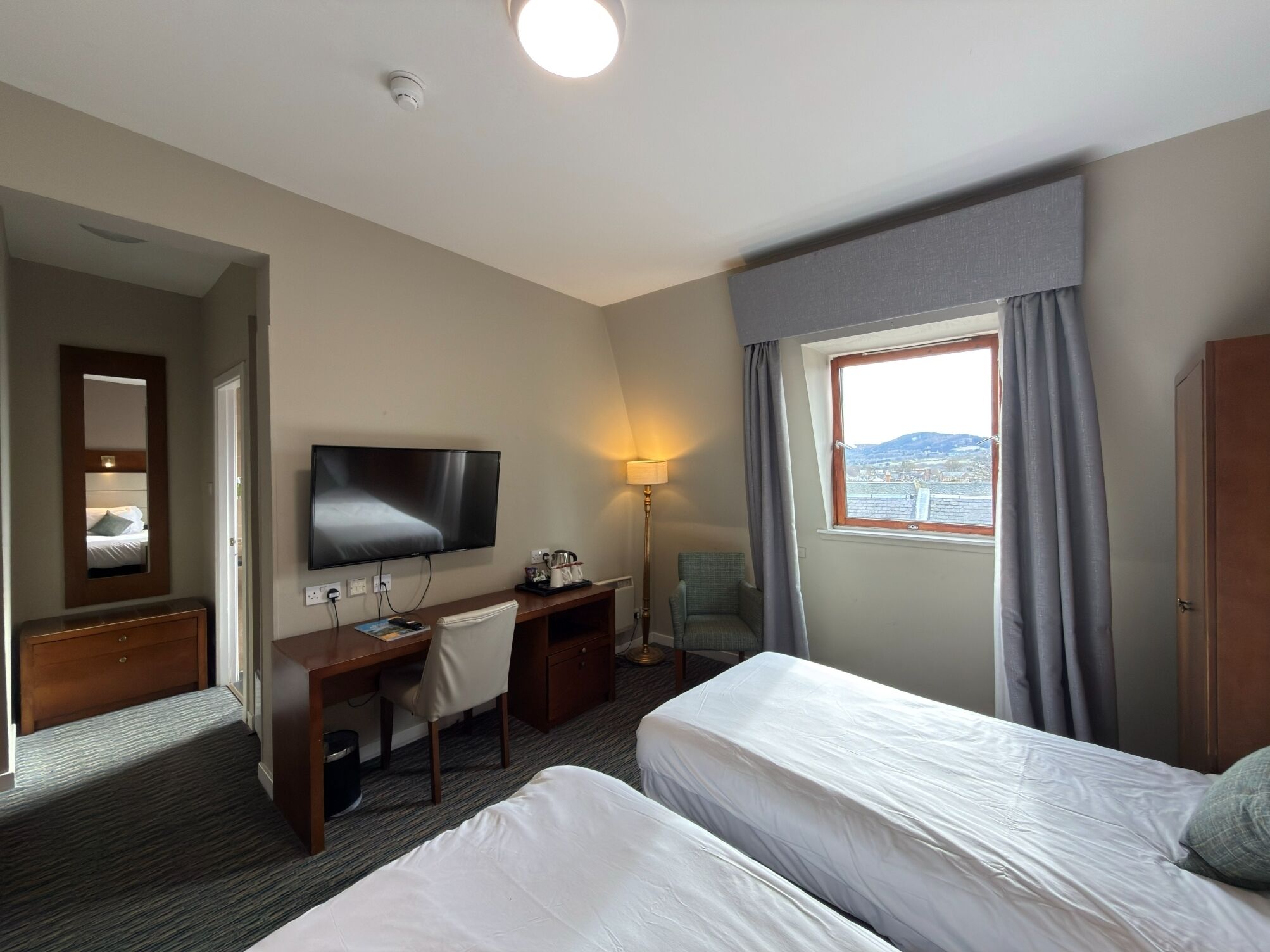A hotel room with a bed, desk, chair, TV, and a window with curtains.