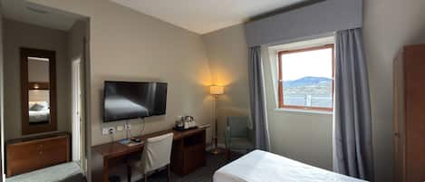 A hotel room with a bed, desk, chair, TV, and a window with curtains.