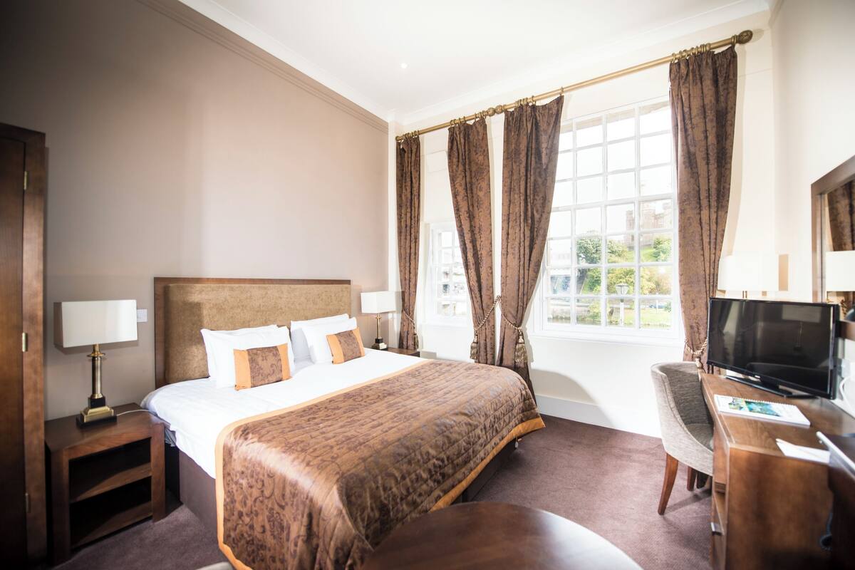 A hotel room with a large bed, a desk with a television, and a window with curtains.