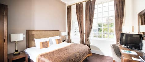 A hotel room with a large bed, a desk with a television, and a window with curtains.