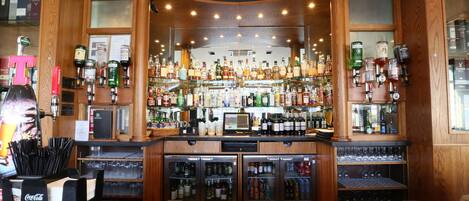 A bar area with shelves of various liquor bottles, a cash register, and a refrigerator stocked with beverages.