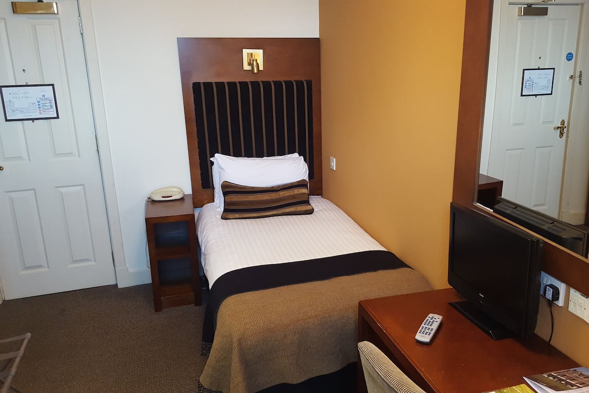 A hotel room with a bed, a desk, a TV, and a mirror.