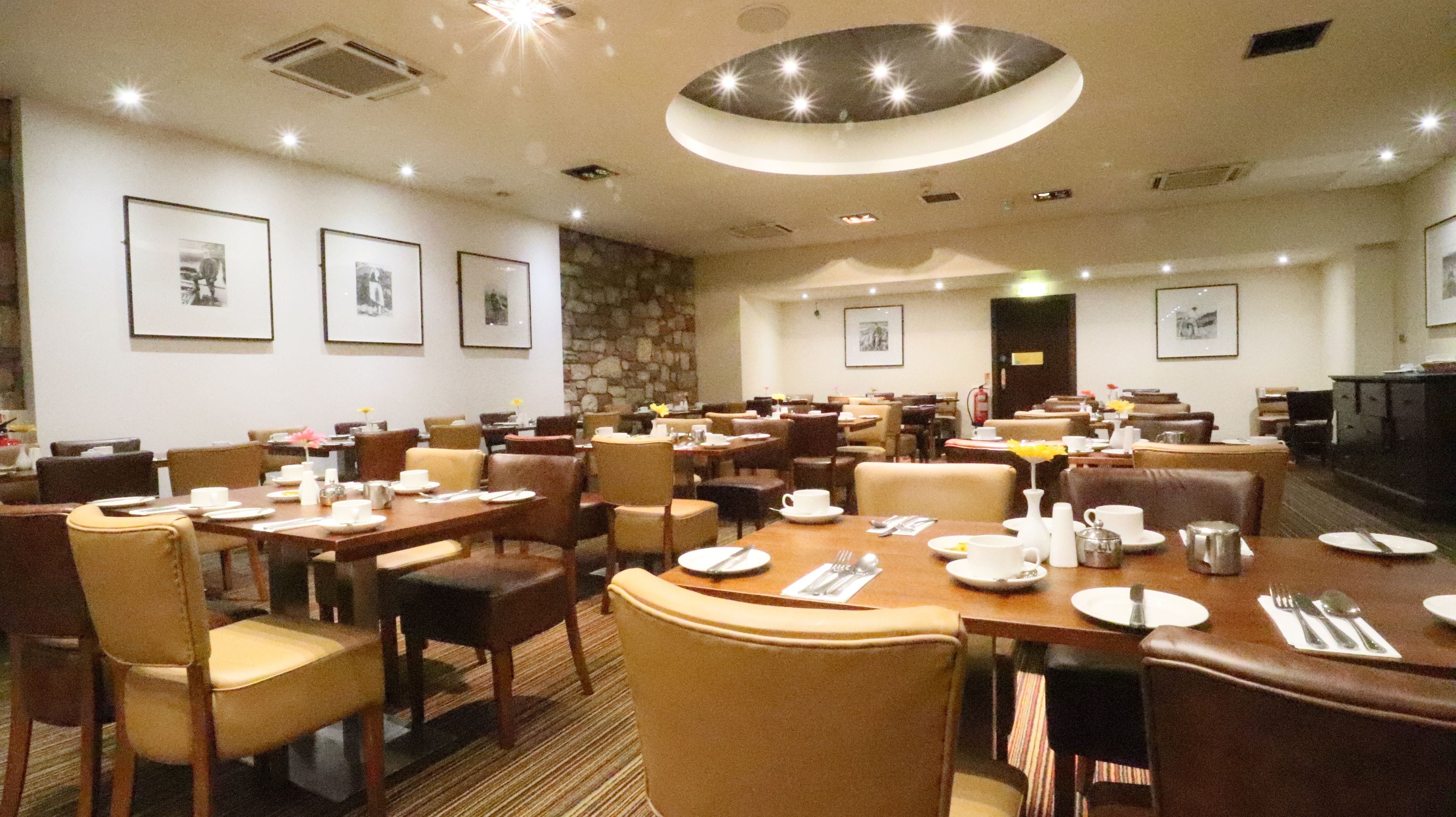En restaurant i et hotel med flere dækketøjsdækkede borde, stole og billeder i rammer på væggene.
