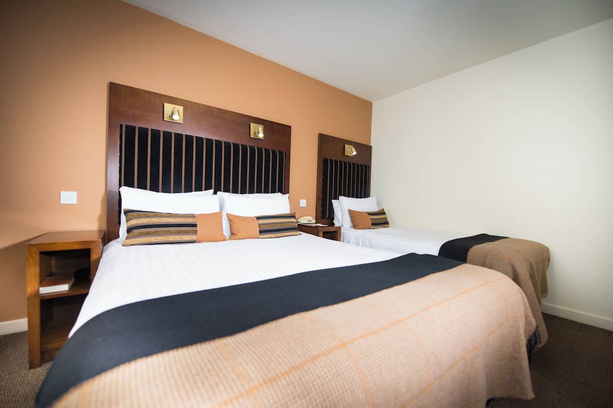 A hotel room with two beds, wooden headboards, and a nightstand with a lamp.