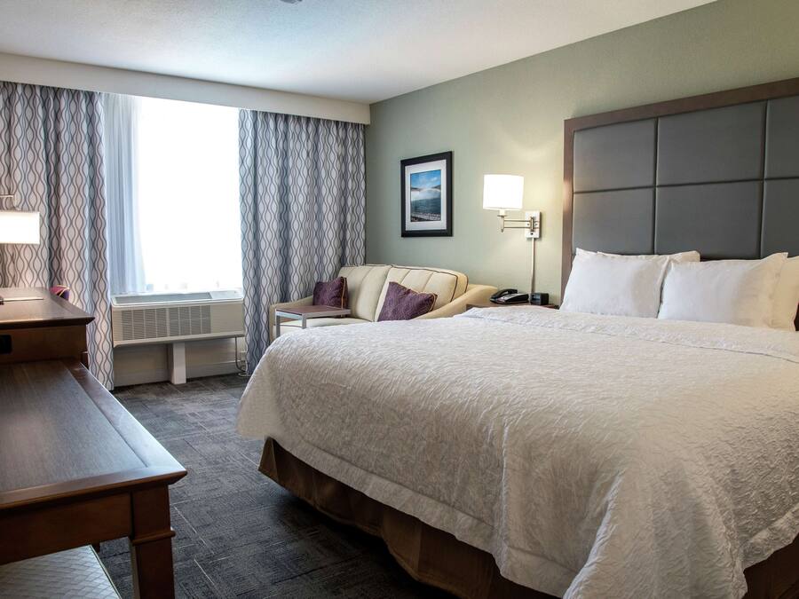 Een hotelkamer met een groot bed, een bureau, een stoel, een televisie en een raam met gordijnen.