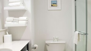 Un baño moderno con inodoro, cabina de ducha de vidrio y lavamanos con toallero.