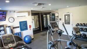 Un gimnasio con cintas de correr, elípticas y un televisor montado en la pared.
