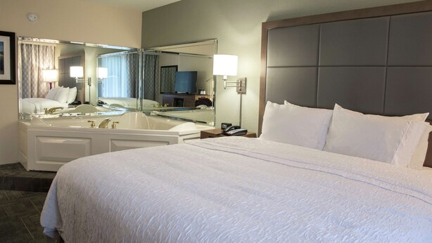 Una habitación de hotel con una cama grande, un baño con bañera, un espejo y una mesita de noche con teléfono.