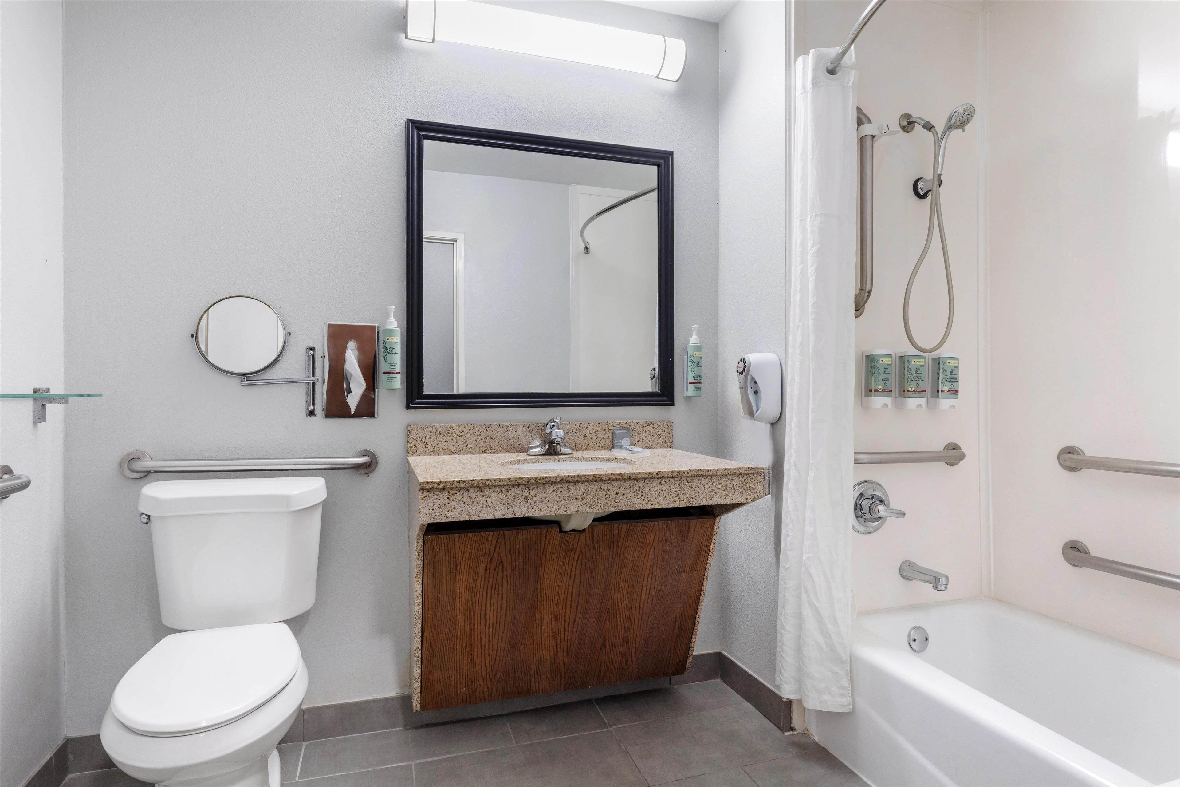 A modern bathroom with a toilet, sink, mirror, shower, and grab bars.