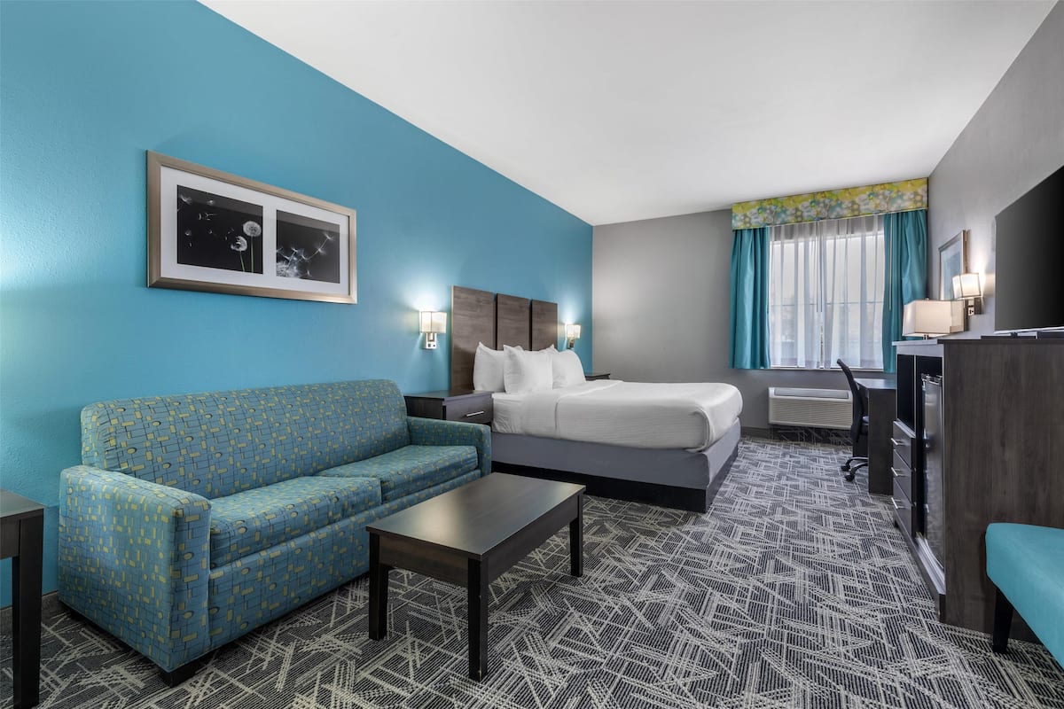 Ein Hotelzimmer mit blauer Wand, einem Bett, einem Schlafsofa, einem Schreibtisch und einem Sessel.