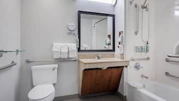 A modern bathroom with a toilet, sink, and bathtub. It includes a mirror, handrails, and a shower area.