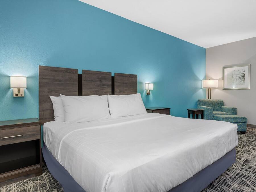 A neatly made bed in a room with a blue accent wall, a wooden headboard, and a small side table with a lamp.