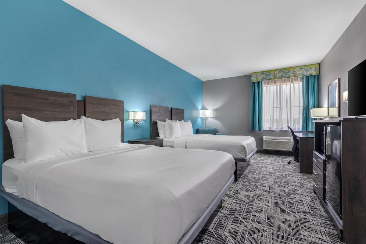 Ein Hotelzimmer mit zwei Betten, einem Schreibtisch, einem Schminktisch und einem Fenster mit Vorhängen.