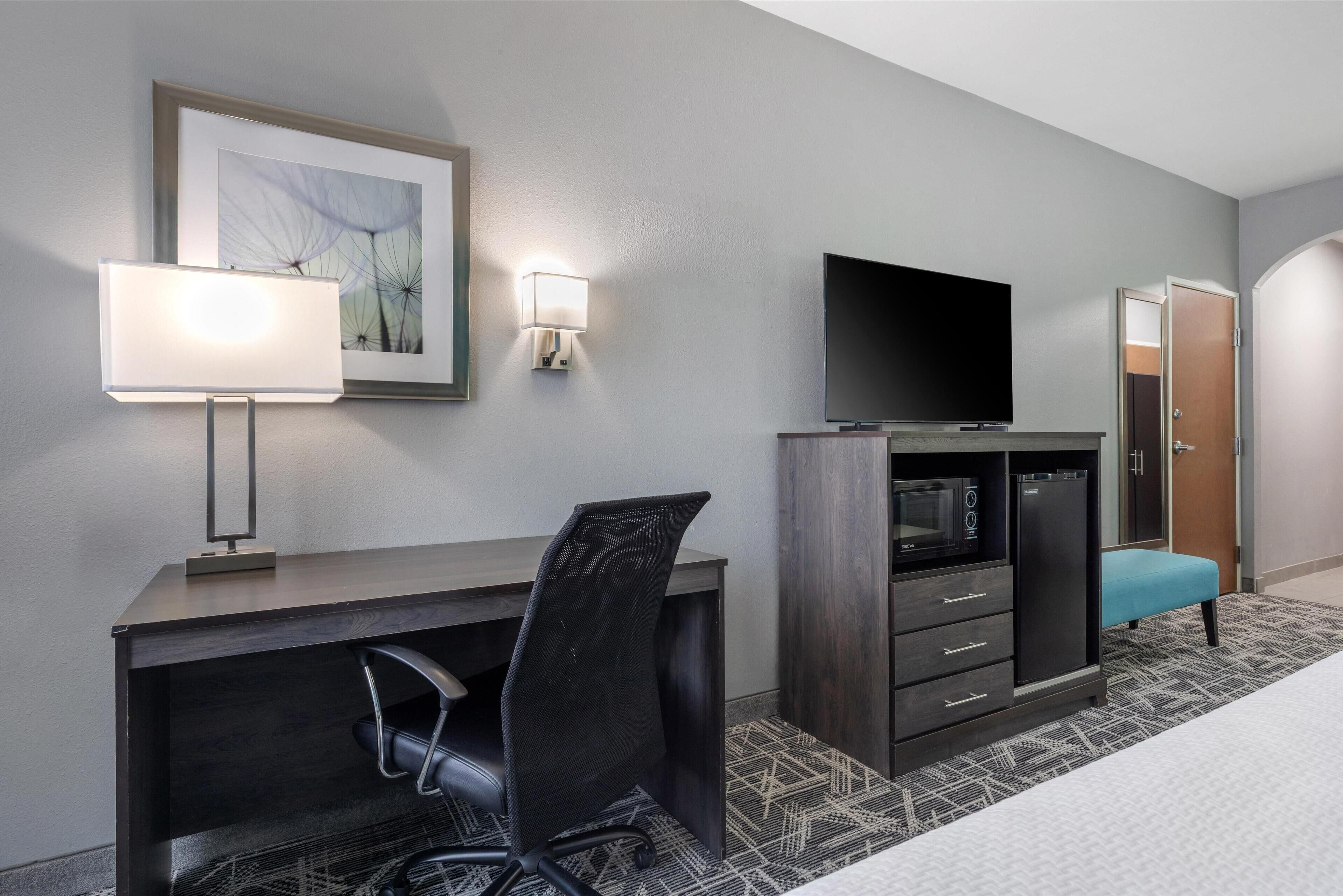 Hotelkamer met een bureau, stoel, televisie, garderobe en een lijst met kunstwerk aan de muur.