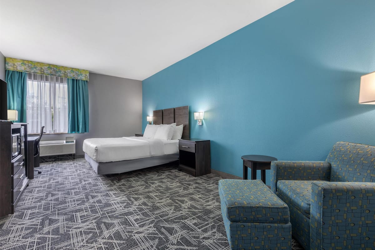Ein Hotelzimmer mit Bett, Nachttischen, einem Schreibtisch, einem Sessel und einem gemusterten Teppich.