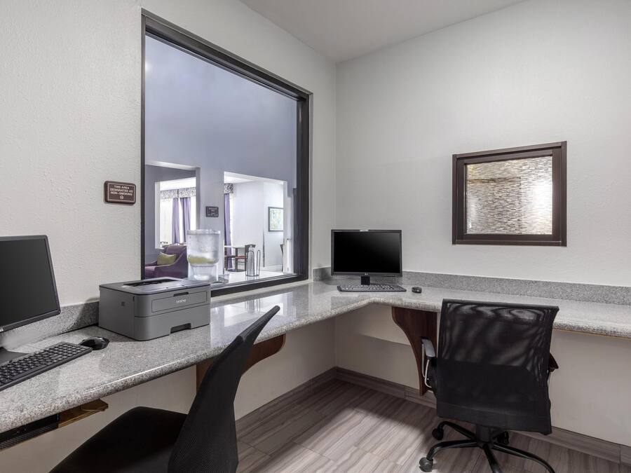 A modern office space with a large window, two monitors, a printer, and a black office chair.