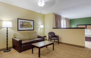Habitación de hotel con sofá, sillón, mesa de centro y un cuadro en la pared.