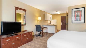 A hotel room with a bed, a TV on a wooden dresser, a desk with a chair, a microwave, and a refrigerator.