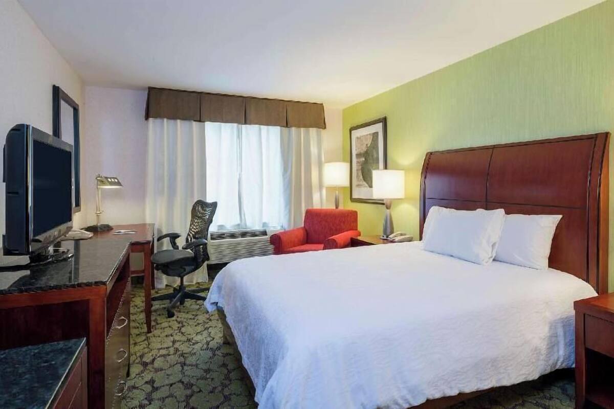 A hotel room with a bed, desk, chair, television, and a window with curtains.
