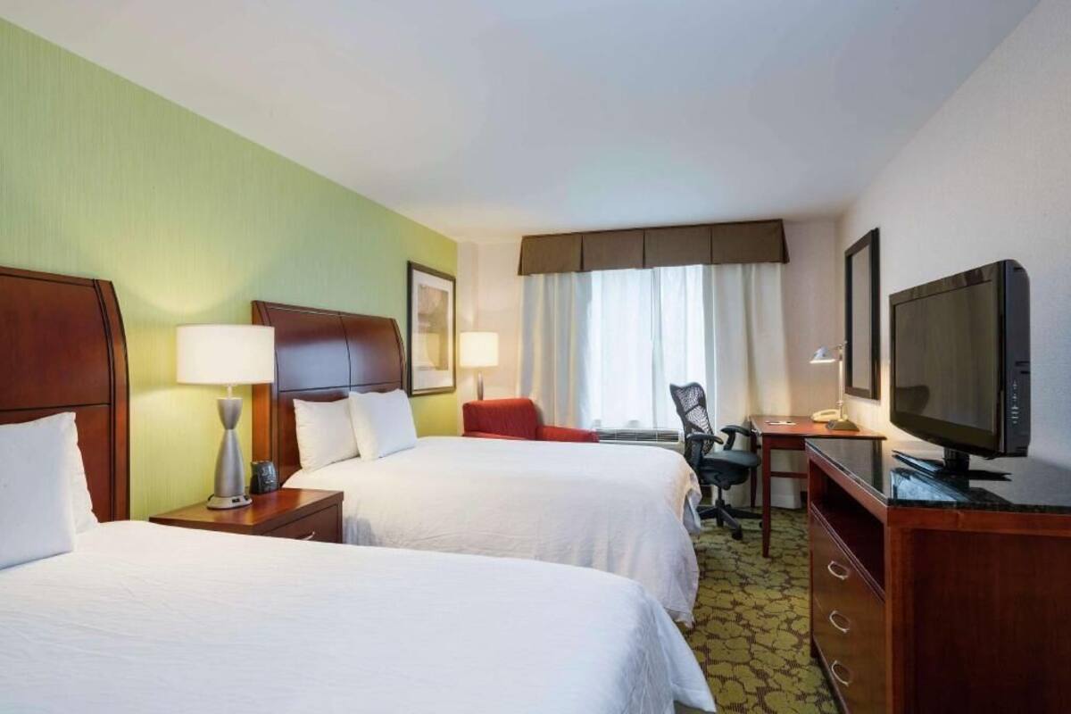 A hotel room with two beds, a desk, a television, and a chair.