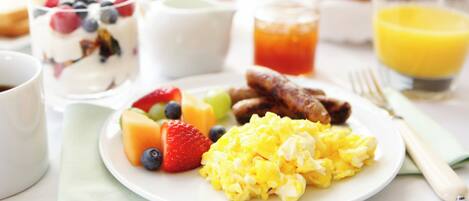 A breakfast plate with scrambled eggs, strawberries, blueberries, and a glass of orange juice.
