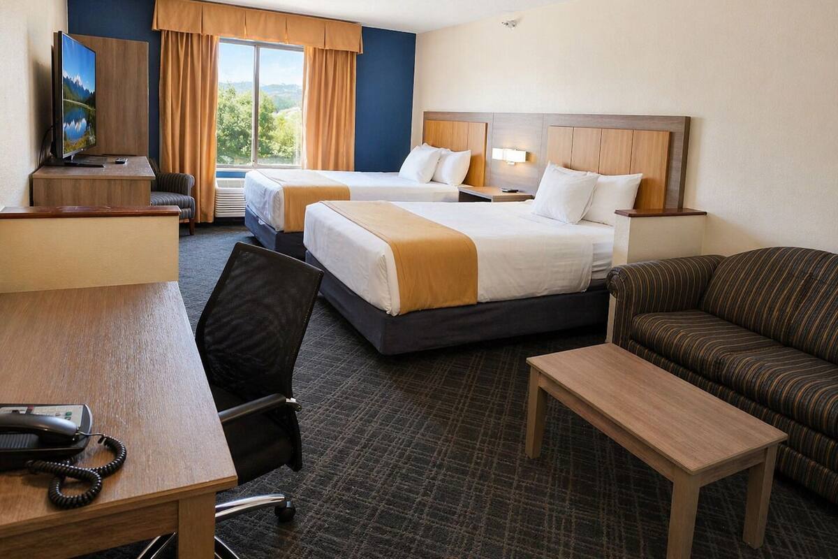 Ein Hotelzimmer mit zwei Betten, einem Schreibtisch, einem Sessel, einer Couch und einem Fernseher.