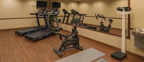 Un gimnasio con cintas de correr, una elíptica, una bicicleta estática, una colchoneta de yoga y un banco para pesas.