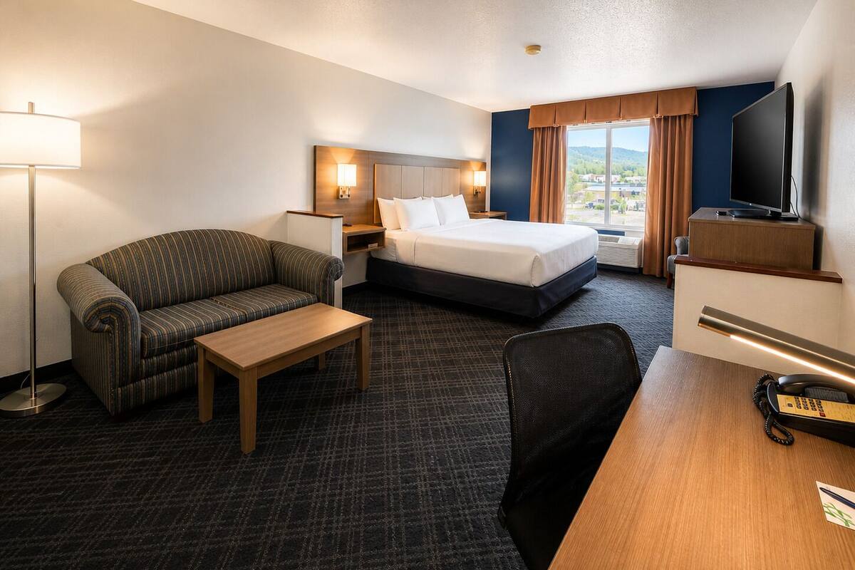 Ein Hotelzimmer mit Bett, Sofa, Schreibtisch, Stuhl, Fernseher und einem Fenster mit Vorhängen.