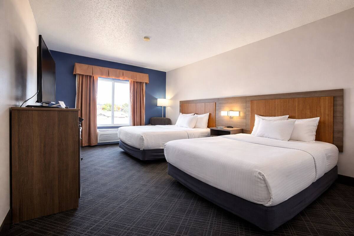Ein Hotelzimmer mit zwei Betten, einem Fernseher, einem Schreibtisch und einem fensterbepflanzten Fenster.