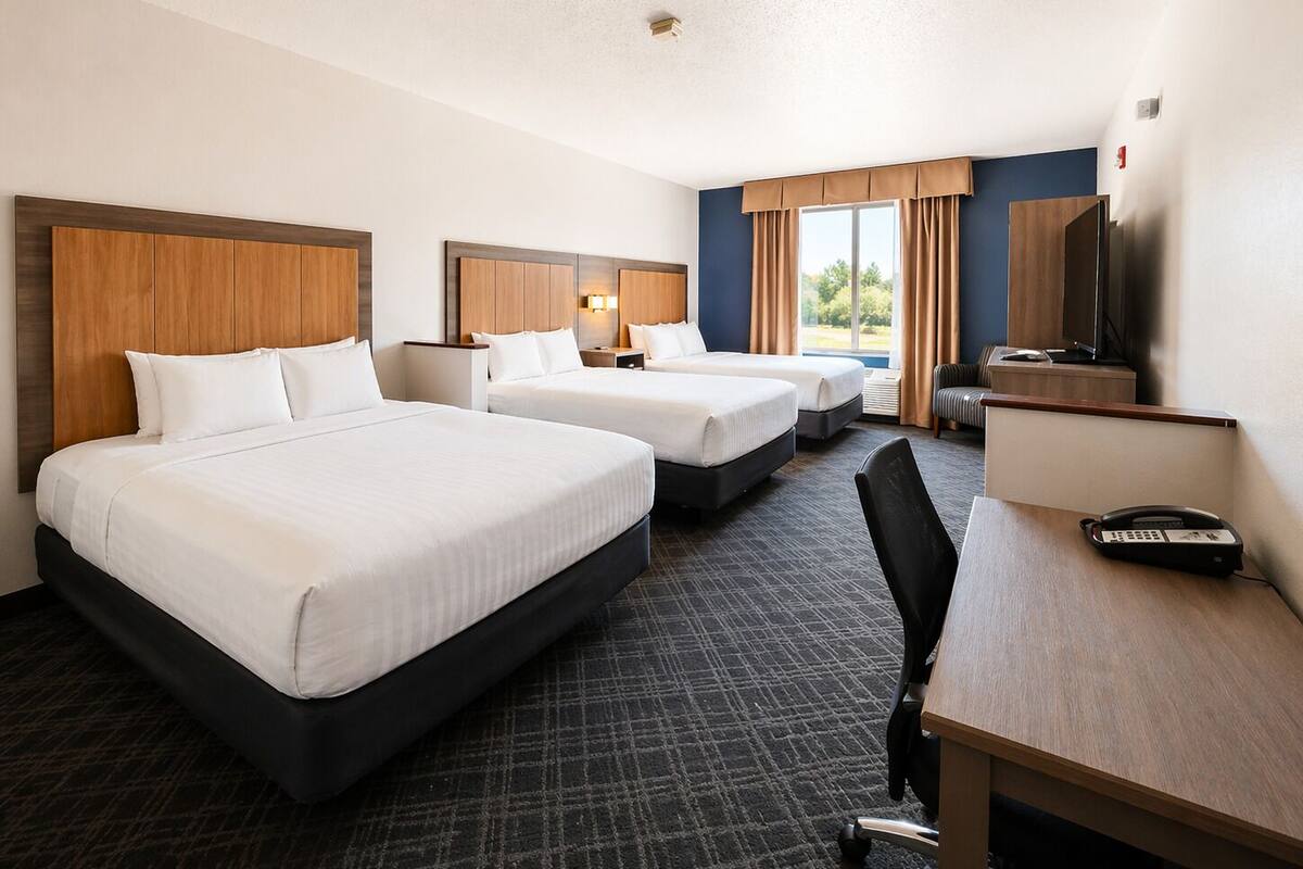 Ein Hotelzimmer mit zwei Betten, einem Schreibtisch, einem Stuhl, einem Fernseher und einem Fenster mit Vorhängen.