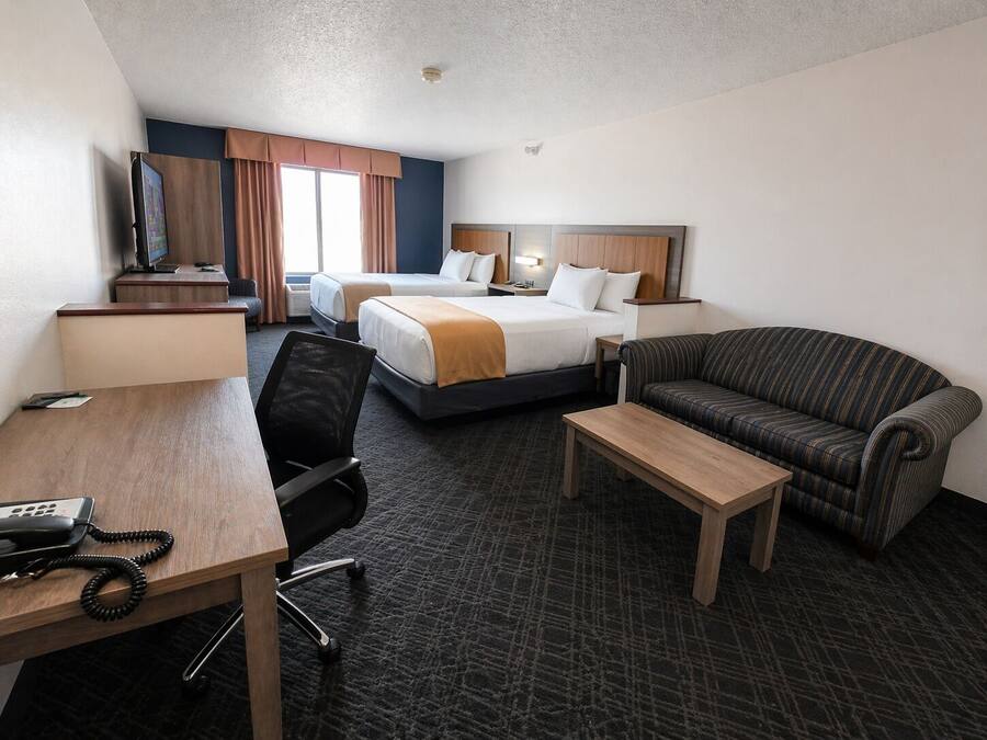 A hotel room with two beds, a desk with a telephone, a chair, a sofa, and a television.