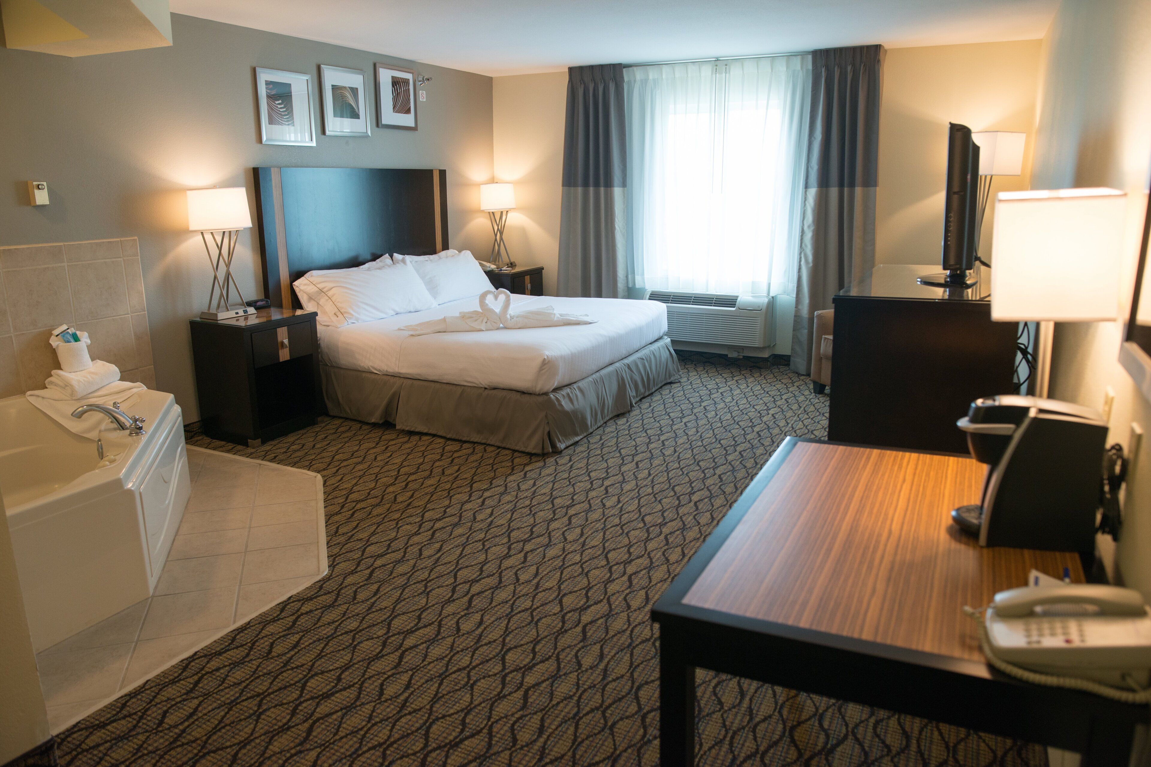 A hotel room with a bed, a desk, a telephone, a television, a bathroom with a bathtub, and a window with curtains.