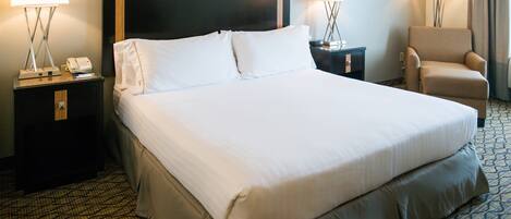 A hotel room with a large bed, two bedside tables with lamps, a chair, and a flat-screen TV on the wall.