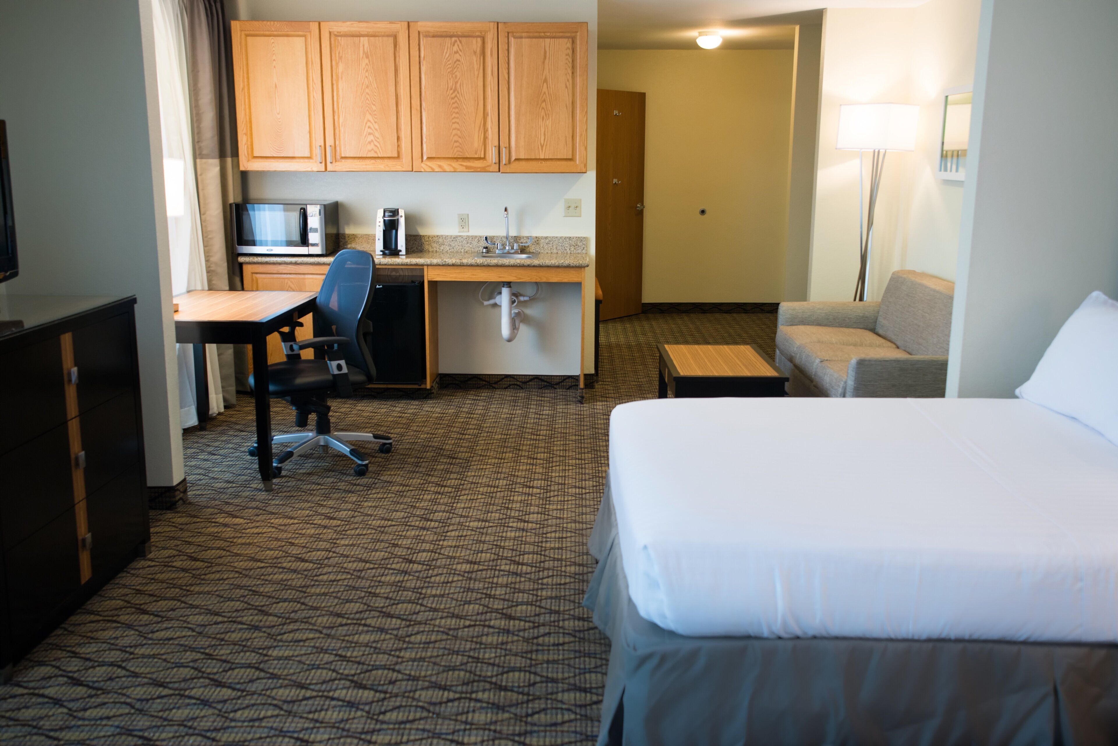 Une chambre d’hôtel comprenant un lit, un bureau avec une chaise, une kitchenette et un canapé.