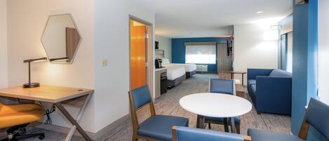Une chambre d’hôtel équipée d’un bureau, de chaises, d’une table ronde, d’un lit et d’une salle de bain.