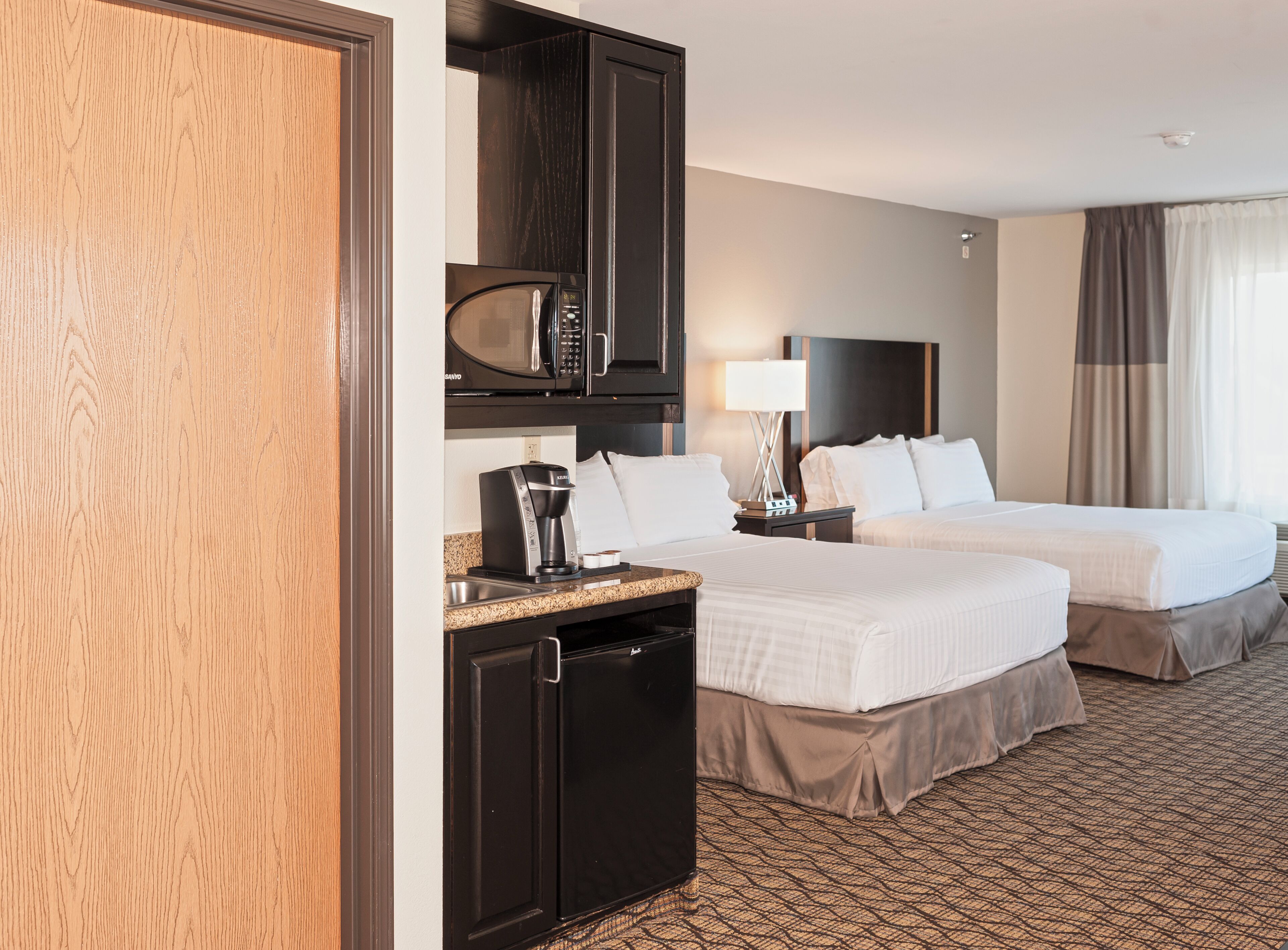 A hotel room with two beds, a microwave, a coffee maker, a nightstand, and a lamp.