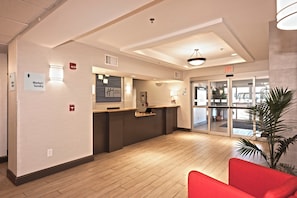 A hotel reception area with a wooden floor, a reception desk, and a glass door leading outside. There are signs for the market/sundry and fire exit. - Holiday Inn Express Hotel & Suites Chanhassen by IHG (Chanhassen)