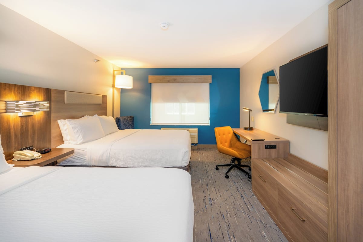 A hotel room with two beds, a desk, a chair, a TV, and a phone on the nightstand.