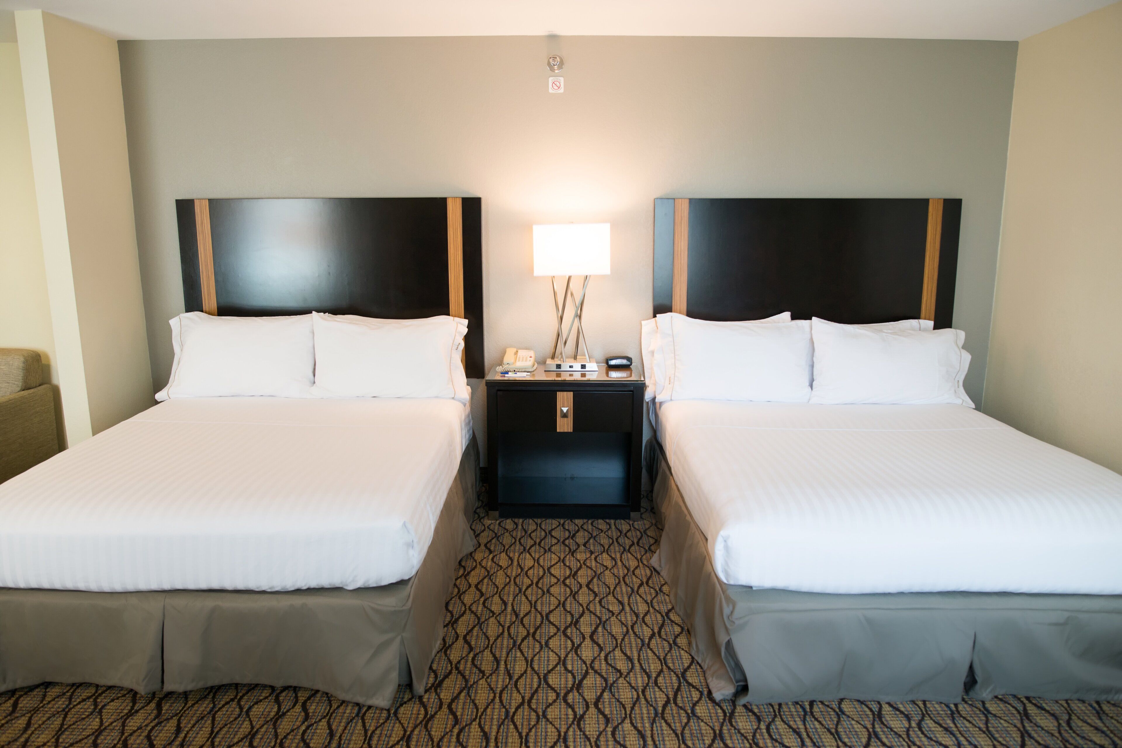 A hotel room with two beds, a nightstand with a lamp, and a patterned carpet.
