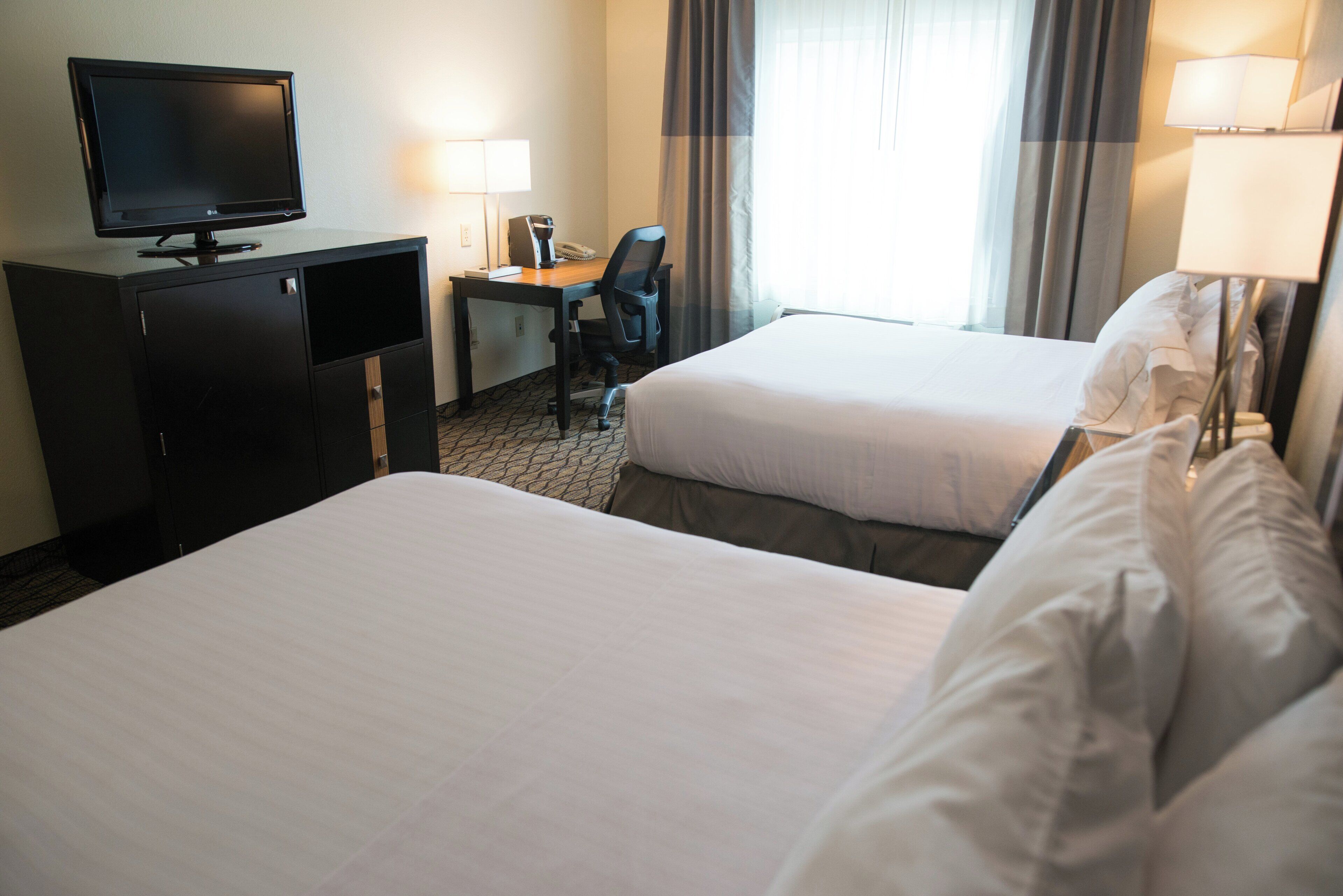 Une chambre d’hôtel avec deux lits, un bureau avec un ordinateur, une télévision et une lampe.
