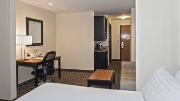 A hotel room with a bed, a desk, a chair, a small table, a mirror, a television, and a door leading to a bathroom.