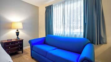Et værelse med en blå sofa, et trænatbord med en lampe og et vindue med gardiner.