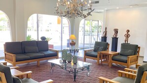 A spacious lobby with a central coffee table surrounded by wooden chairs and sofas, large windows with arched tops, and a chandelier. - Hotel Americana (Nogales)
