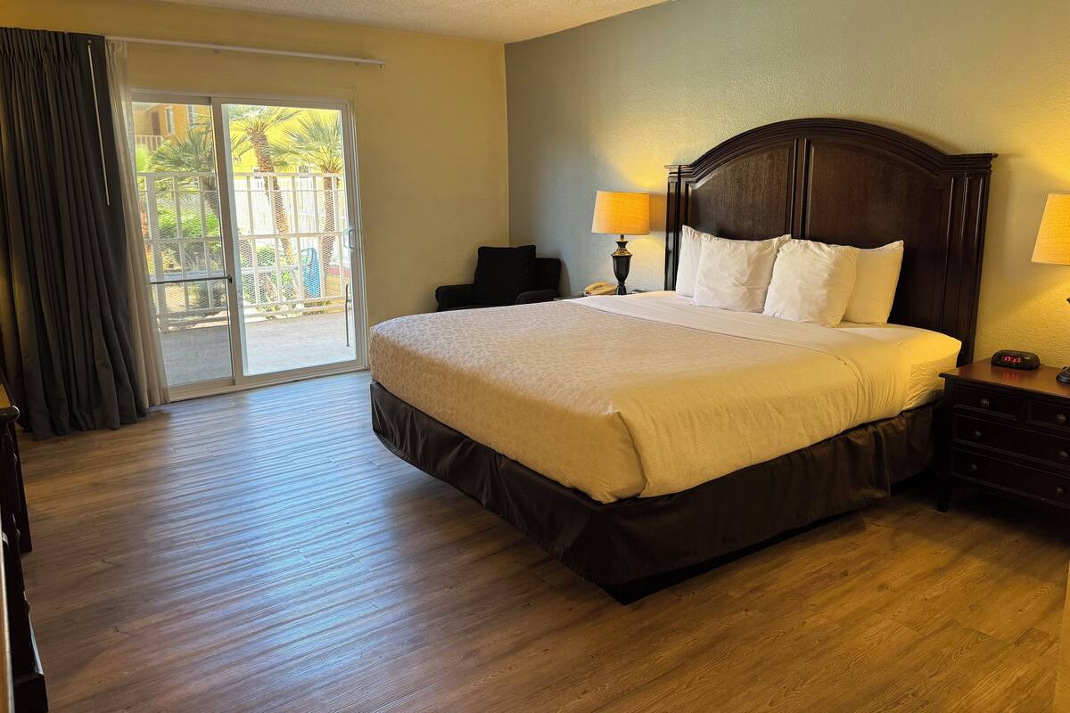 Een hotelkamer met een groot bed, twee bedlampen, een nachtkastje en een schuifdeur naar een buitenruimte.