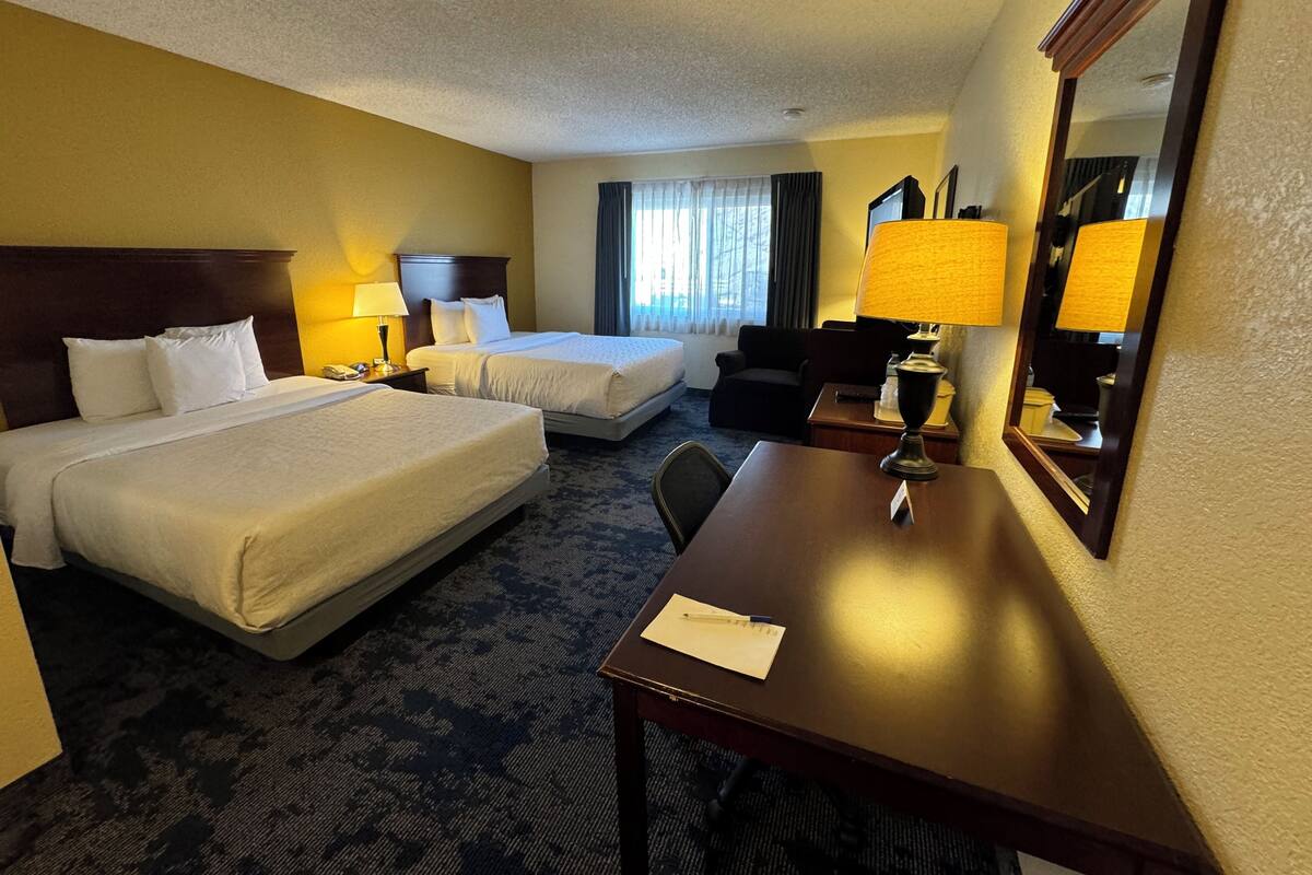 Een hotelkamer met twee bedden, een bureau, een stoel, een lamp en een spiegel.