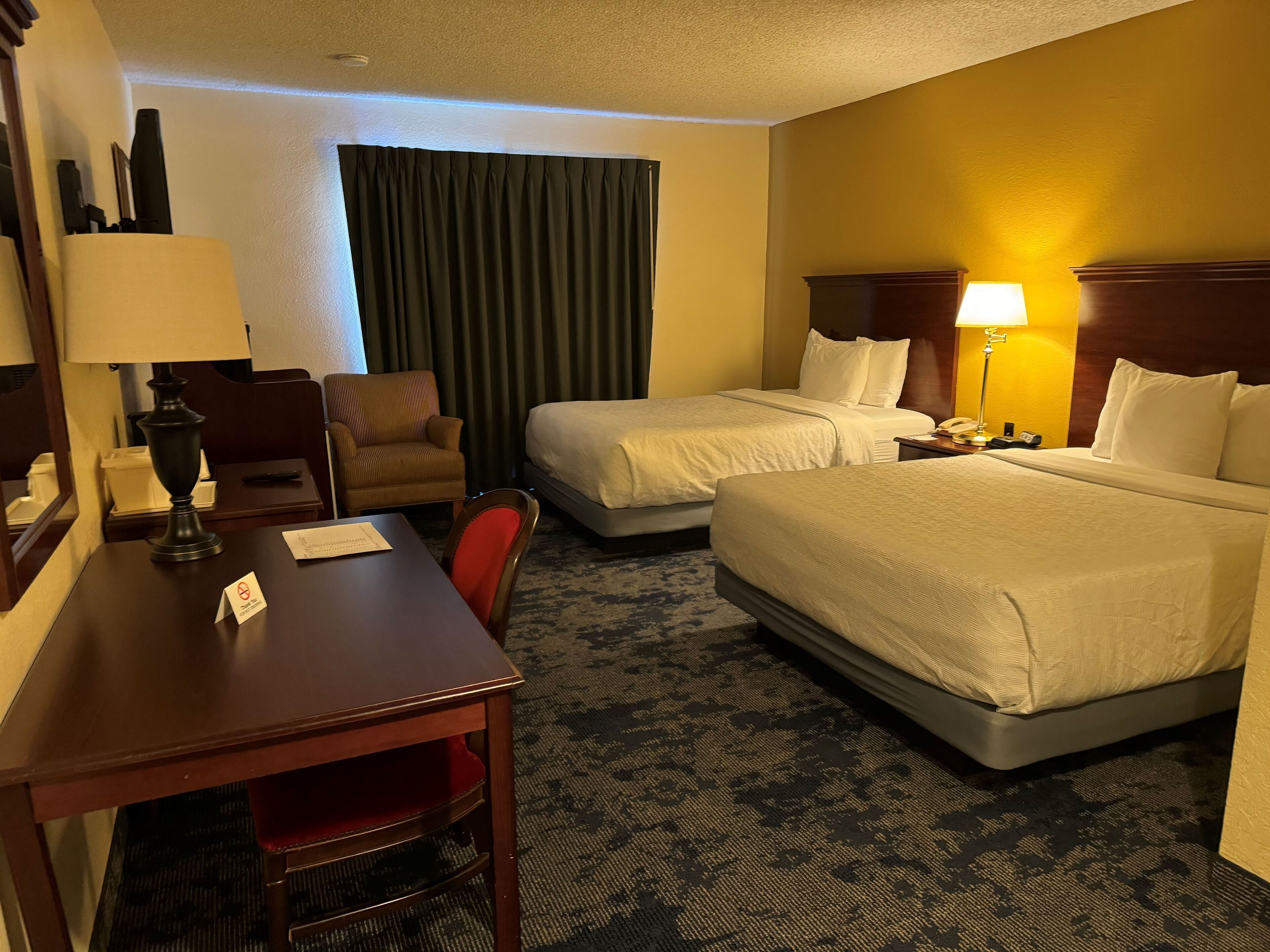 A hotel room with two beds, a desk, a chair, a lamp, and a nightstand.