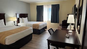 Ein Hotelzimmer mit zwei Betten, einem Schreibtisch, einem Stuhl, einer Lampe, einem Fenster mit Vorhängen und einem Spiegel.