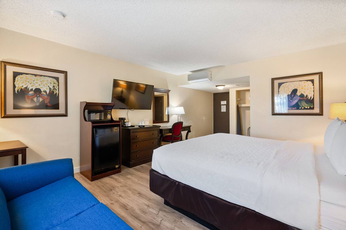 Een hotelkamer met een groot bed, een bureau met stoel, een kast en twee foto's in lijsten aan de muur.